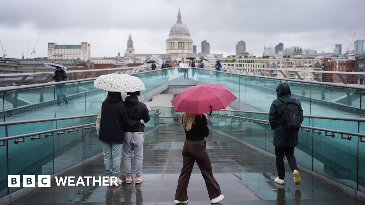 People with umbrellas walking along the Millennium Bridge, in London, during a rain shower